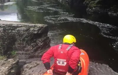Individual in a red kayak preparing to enter the water beside a rocky riverbank.