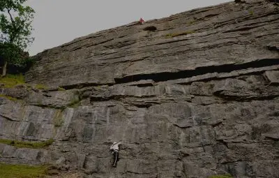 A climber ascending a vertical rock face while another climber is positioned above on a cliff.