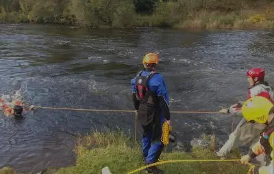 Rescue team member in a wetsuit assisting a swimmer in a river during a rescue operation.