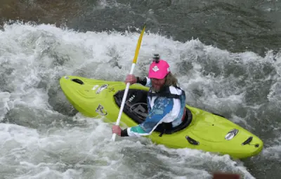 A kayaker in a bright yellow kayak navigating through white water rapids wearing a pink cap.