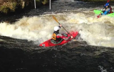 A kayaker in a red kayak paddling through turbulent water in a river.
