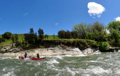 Two individuals paddling a red canoe on a river with rocky banks and greenery in the background.