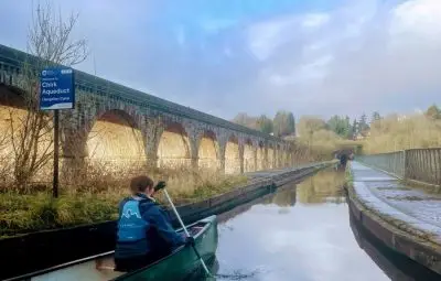 Person paddling a canoe on the Chrick Aqueduct with stone arches in the background.
