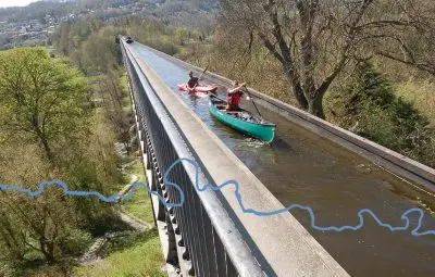 Two canoes navigating a waterway on a large aqueduct surrounded by trees.
