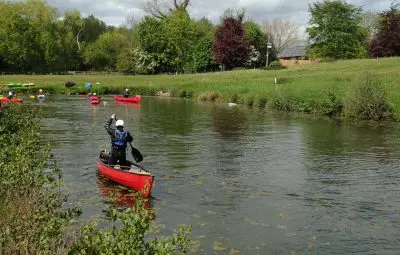 A person paddling a red canoe on a river surrounded by greenery and trees.