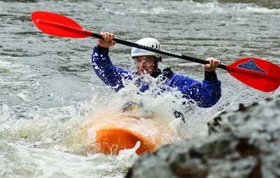 Individual paddling an orange kayak through turbulent water with a double-bladed paddle.