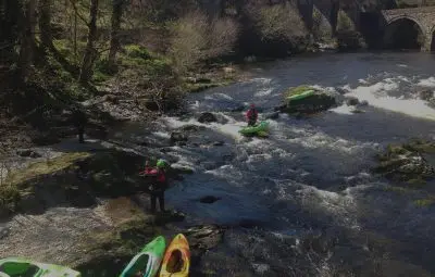 Group of kayakers preparing to navigate a river with rocky banks and flowing water.