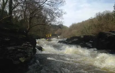 A group of people rafting on a river with visible rapids and rocky banks.
